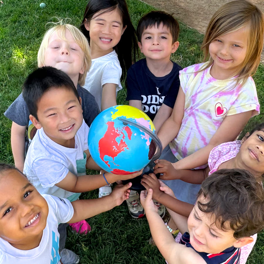 Scripps Montessori children gathered around a globe on the school lawn